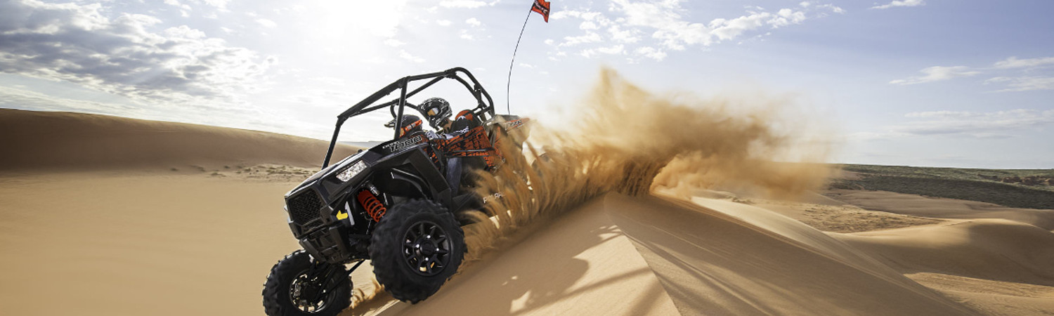 Two people on a 2022 Polaris® side by side riding on some sand dunes.